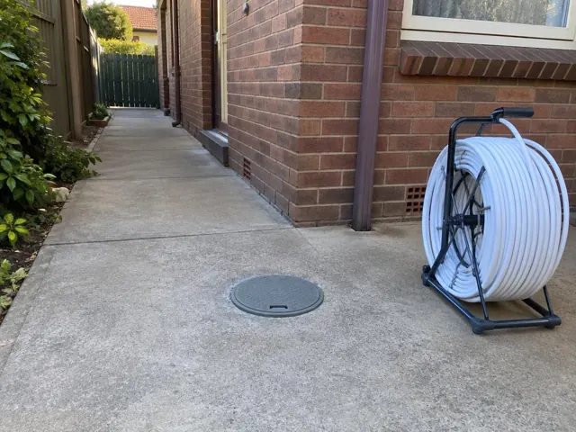 Flush round access cover in a concrete side path beside a brick house in Lidcombe